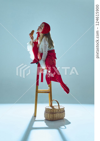 Young woman in white lace dress and red accents reclining on stool, lifting bread to lips, merging hunger with seduction. Young woman in white lace dress and red accents reclining on stool, lifting bread to lips, merging hunger with seduction. 124615900