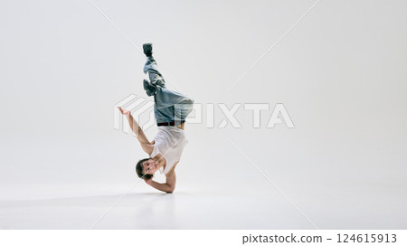 Breakdancer, dressed casual attire, holding extreme one-hand freeze with legs extended in mid-air against white background. Breakdancer, dressed casual attire, holding extreme one-hand freeze with legs extended in mid-air against white background. 124615913