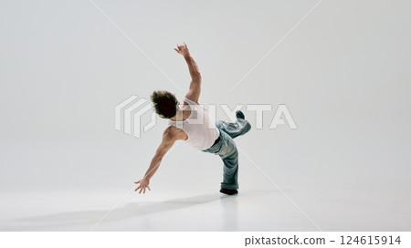 Freestyle dancer, dressed casual outfit, pushing off ground in energetic power move with artistic fluidity against white background. Freestyle dancer, dressed casual outfit, pushing off ground in energetic power move with artistic fluidity against white background. 124615914