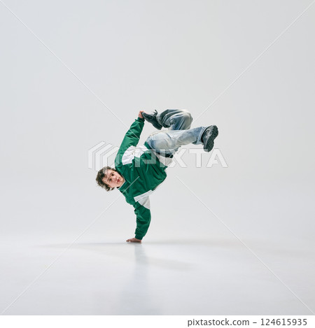 Dance performer, dressed retro outfit, balancing on one hand while executing stylish breakdance move against white studio setting. 124615935