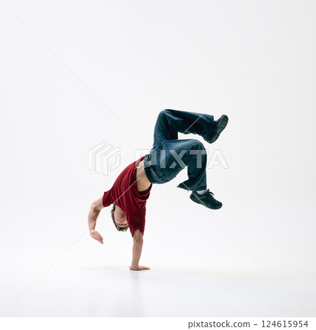 Young breakdancer flipping mid-air, his body arched against white studio background, motion captured in perfect form. Young breakdancer flipping mid-air, his body arched against white studio background, motion captured in perfect form. 124615954