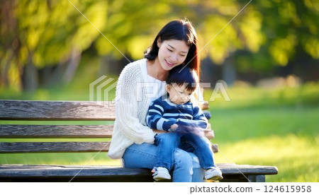 A mother sitting on a park bench holding a baby boy 124615958