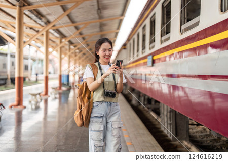 Engagement and Discovery. A woman checking her phone with a bag and camera at a vibrant train station. 124616219