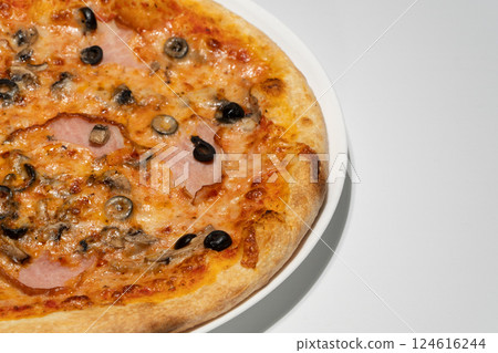 Close-up of Freshly Baked Pizza with Olives, Ham and Crispy Thin Crust Served on White Plate Close-up of Freshly Baked Pizza with Olives, Ham and Crispy Thin Crust Served on White Plate 124616244