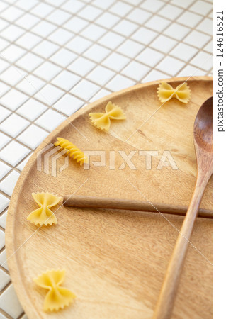 time to eat pasta. wooden plate with fork and spoon in form of clock hands. pasta on plate. time to eat pasta. wooden plate with fork and spoon in form of clock hands. pasta on plate. 124616521