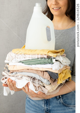 mockup, a happy woman holds a stack of clothes and a laundry gel or conditioner for washing clothes. mockup, a happy woman holds a stack of clothes and a laundry gel or conditioner for washing clothes. 124616526