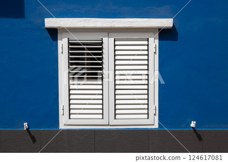 Bright blue wall and white window with shutter, Spain 124617081
