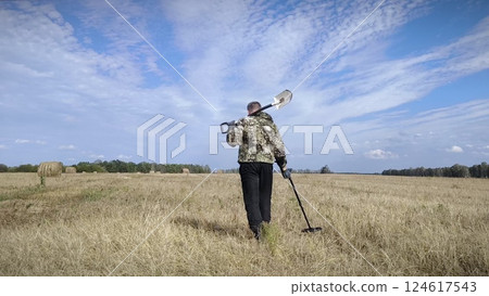 man in a field with a metal detector. treasure hunter searches for valuable metal using a metal detector. Treasure hunt concept. 124617543
