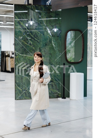 Woman in white coat holding tablet in interior design showroom Woman in white coat holding tablet in interior design showroom 124618417