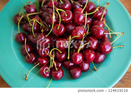 A vibrant pile of ripe red cherries sits on a teal plate, showcasing their juicy freshness A vibrant pile of ripe red cherries sits on a teal plate, showcasing their juicy freshness 124619216
