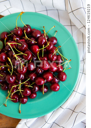 A teal plate holds a mound of glistening, ripe red cherries, their stems vibrant against the smooth, glazed surface A teal plate holds a mound of glistening, ripe red cherries, their stems vibrant against the smooth, glazed surface 124619219