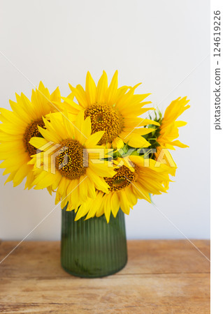 Vibrant sunflowers in a ribbed green vase brighten a rustic wooden table 124619226