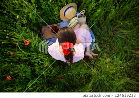 A young woman enjoys a tranquil picnic amidst a vibrant poppy field, surrounded by nature's beauty 124619238