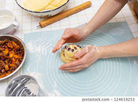 A young Caucasian woman's hands carefully shape a sweet Easter bread roll, filled with dried fruit. The festive pastry is almost ready for baking A young Caucasian woman's hands carefully shape a sweet Easter bread roll, filled with dried fruit. The festive pastry is almost ready for baking 124619253