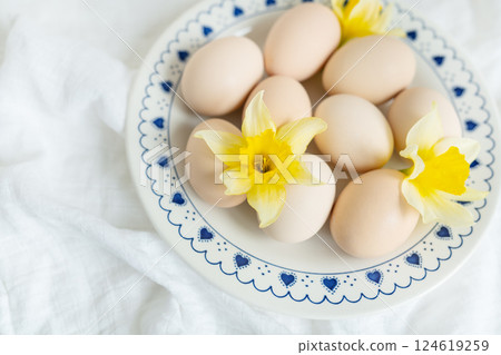 Pastel-colored eggs nestled amongst delicate daffodils on a charming blue and white plate. A perfect springtime Easter image, symbolizing new beginnings and celebration 124619259
