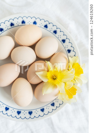 Pastel eggs and cheerful daffodils create a lovely Easter scene on a blue and white plate. The image captures the freshness and joy of spring 124619260