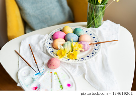 Pastel Easter eggs, daffodils, and paintbrushes are artfully arranged on a white table. This image evokes spring and the joyful celebration of Easter Pastel Easter eggs, daffodils, and paintbrushes are artfully arranged on a white table. This image evokes spring and the joyful celebration of Easter 124619261