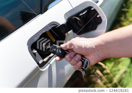 A hand inserts a car key into the fuel filler flap of a white diesel vehicle 124619281
