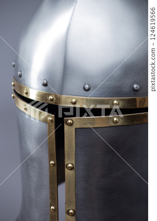 Silver Medieval Barbute Helmet with Brass Trim. This image shows a shiny silver helmet with a distinctive T-shaped opening for the face, accented with brass trim and rivets. Silver Medieval Barbute Helmet with Brass Trim. This image shows a shiny silver helmet with a distinctive T-shaped opening for the face, accented with brass trim and rivets. 124619566