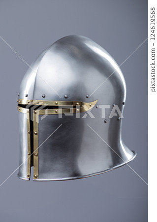 Silver Medieval Barbute Helmet with Brass Trim. This image shows a shiny silver helmet with a distinctive T-shaped opening for the face, accented with brass trim and rivets. Silver Medieval Barbute Helmet with Brass Trim. This image shows a shiny silver helmet with a distinctive T-shaped opening for the face, accented with brass trim and rivets. 124619568
