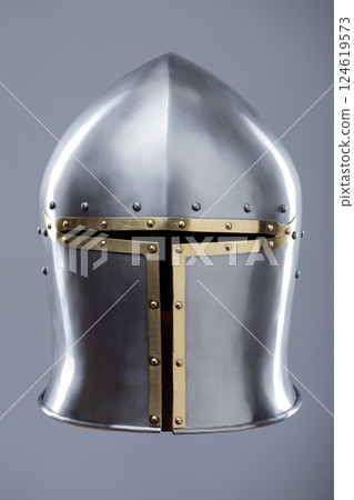 Silver Medieval Barbute Helmet with Brass Trim. This image shows a shiny silver helmet with a distinctive T-shaped opening for the face, accented with brass trim and rivets. Silver Medieval Barbute Helmet with Brass Trim. This image shows a shiny silver helmet with a distinctive T-shaped opening for the face, accented with brass trim and rivets. 124619573