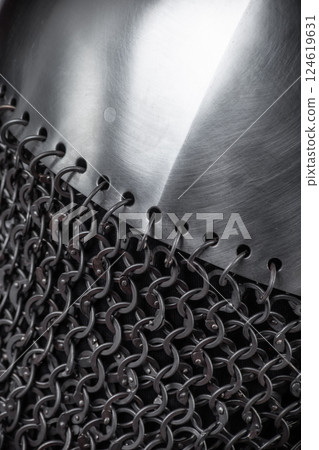Close-Up of Metal Plate Attached to Chainmail. Detailed view showing the connection between a solid steel plate and interlinked mail rings. Close-Up of Metal Plate Attached to Chainmail. Detailed view showing the connection between a solid steel plate and interlinked mail rings. 124619631
