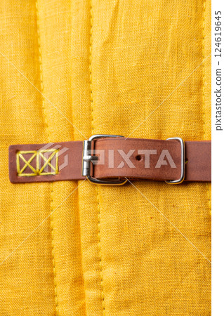 Close-up of Leather Strap and Buckle on Yellow Gambeson. Detailed view of medieval armor fastening. Close-up of Leather Strap and Buckle on Yellow Gambeson. Detailed view of medieval armor fastening. 124619645