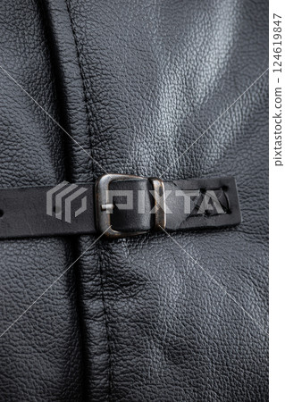 Close-Up of Leather Jacket Buckle. This image shows a close-up of a silver buckle on a black leather strap, which is part of the sleeveless jacket. The buckle has a classic rectangular shape with a Close-Up of Leather Jacket Buckle. This image shows a close-up of a silver buckle on a black leather strap, which is part of the sleeveless jacket. The buckle has a classic rectangular shape with a 124619847