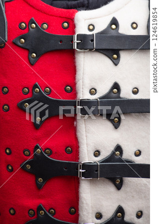 Close-Up of Red and White Brigandine Armor Details. This image provides a detailed close-up of the red and white brigandine armor, showcasing the brass-colored studs, black leather straps with silver 124619854