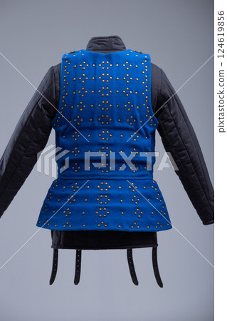 Bright Blue Brigandine Armor with Studs and Black Straps. This image shows a bright blue brigandine armor, featuring rows of small brass-colored studs and secured with multiple black leather straps 124619856