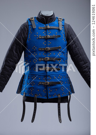 Bright Blue Brigandine Armor with Studs and Black Straps. This image shows a bright blue brigandine armor, featuring rows of small brass-colored studs and secured with multiple black leather straps 124619861
