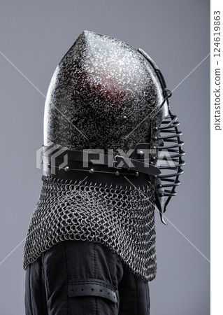 Dark Helmet with Ribbed Faceplate and Chainmail. This image shows a dark, possibly blackened steel, helmet with a pointed top and a distinctive faceplate featuring a series of horizontal ribs. A 124619863