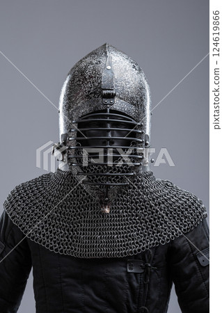 Dark Helmet with Ribbed Faceplate and Chainmail. This image shows a dark, possibly blackened steel, helmet with a pointed top and a distinctive faceplate featuring a series of horizontal ribs. A Dark Helmet with Ribbed Faceplate and Chainmail. This image shows a dark, possibly blackened steel, helmet with a pointed top and a distinctive faceplate featuring a series of horizontal ribs. A 124619866