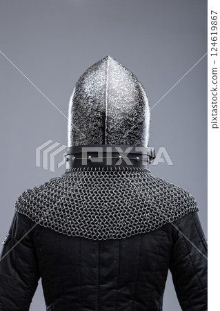 Dark Metal Helmet with Pointed Top and Faceplate. This image shows a dark metal helmet with a pointed top and a faceplate that covers the lower part of the face, featuring several horizontal slits for 124619867
