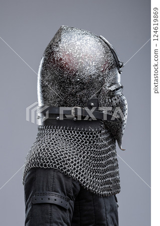 Dark Metal Helmet with Pointed Top and Faceplate. This image shows a dark metal helmet with a pointed top and a faceplate that covers the lower part of the face, featuring several horizontal slits for 124619869