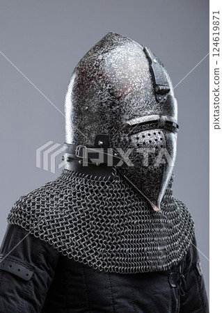 Dark Metal Helmet with Pointed Top and Faceplate. This image shows a dark metal helmet with a pointed top and a faceplate that covers the lower part of the face, featuring several horizontal slits for 124619871