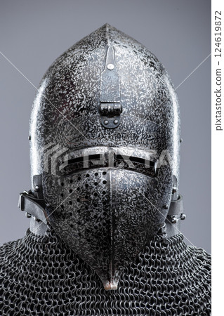 Dark Metal Helmet with Pointed Top and Faceplate. This image shows a dark metal helmet with a pointed top and a faceplate that covers the lower part of the face, featuring several horizontal slits for 124619872