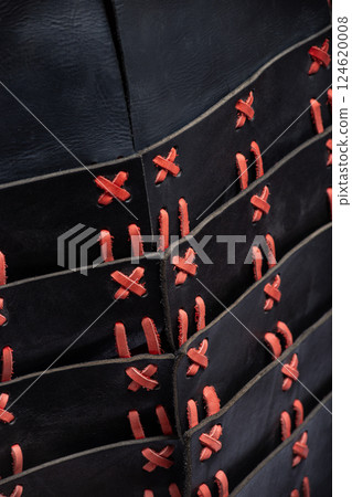 Close-up of Black and Red Leather Armor Lacing. Detailed view of the intricate red lacing connecting the black leather plates of the medieval cuirass. Close-up of Black and Red Leather Armor Lacing. Detailed view of the intricate red lacing connecting the black leather plates of the medieval cuirass. 124620008
