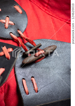 Close-up of Black and Red Leather Shoulder Armor. Detailed view of the mannequin's shoulder armor featuring black leather and contrasting red lacing. 124620010