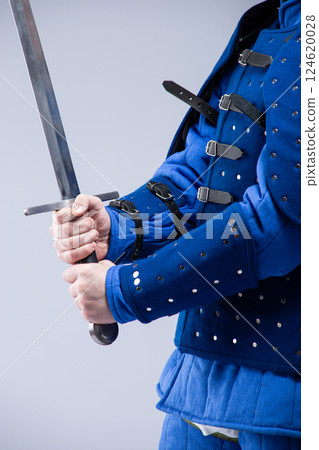 Hands Gripping Sword in Blue Armor. Close-up of medieval fighter holding a sharp weapon. Hands Gripping Sword in Blue Armor. Close-up of medieval fighter holding a sharp weapon. 124620028