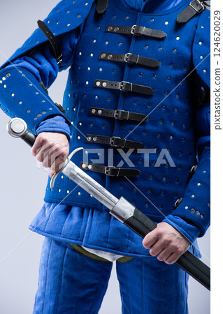 Blue Brigandine Armor with Sword. Medieval torso protection featuring metal plates and leather straps. Blue Brigandine Armor with Sword. Medieval torso protection featuring metal plates and leather straps. 124620029