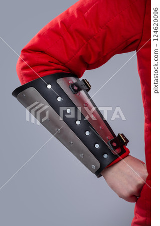 Close-Up of Silver Splinted Bracers on Red Padded Armor. This image shows a close-up of silver metal splinted bracers worn over a red padded garment, likely a gambeson. The bracers are attached with 124620096