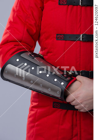 Close-Up of Silver Splinted Bracers on Red Padded Armor. This image shows a close-up of silver metal splinted bracers worn over a red padded garment, likely a gambeson. The bracers are attached with 124620097