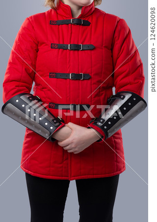 Red Quilted Gambeson with Black Leather Straps. This image shows a red quilted gambeson, a type of padded armor, with black leather straps and silver buckles down the front. 124620098