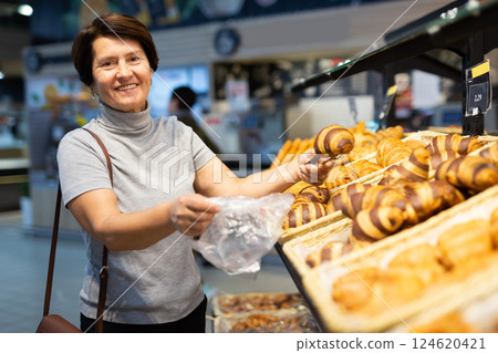 Mature woman chooses hot fresh sweet buns at supermarket showcase 124620421