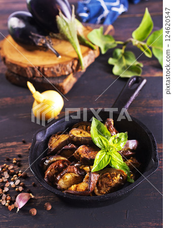 Fried eggplant in a pan. Cooking fried eggplant. Culinary tools, wooden board, knife, fork and spice Fried eggplant in a pan. Cooking fried eggplant. Culinary tools, wooden board, knife, fork and spice 124620547