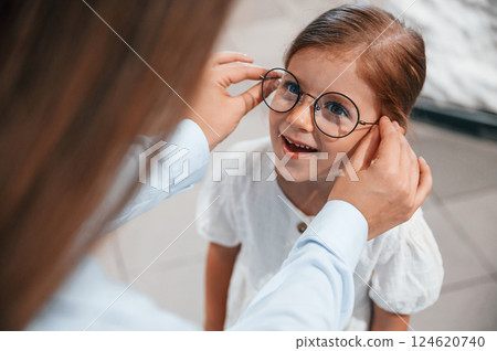 Wearing new eyewear. Woman and girl is in the glasses store Wearing new eyewear. Woman and girl is in the glasses store 124620740