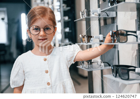 Cute customer. Little girl in the glasses store choosing eyewear Cute customer. Little girl in the glasses store choosing eyewear 124620747