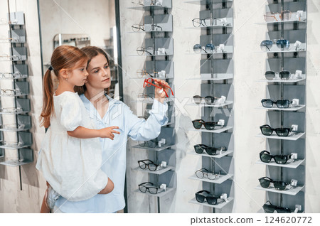 Mother and daughter. Woman and girl is in the glasses store choosing eyewear together 124620772