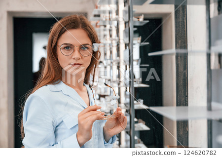 Portrait of woman that is with glasses in the store. Choosing right eyewear for correcting vision Portrait of woman that is with glasses in the store. Choosing right eyewear for correcting vision 124620782